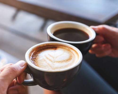Closeup image of a man and a woman clinking white coffee mugs in cafe Closeup image of a man and a woman clinking white coffee mugs in cafe
